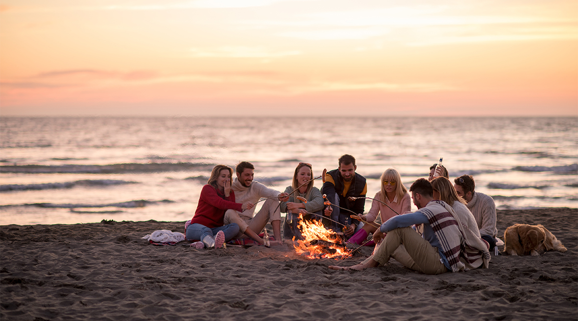 Group of friends sitting around a campfire on the beach at sunset